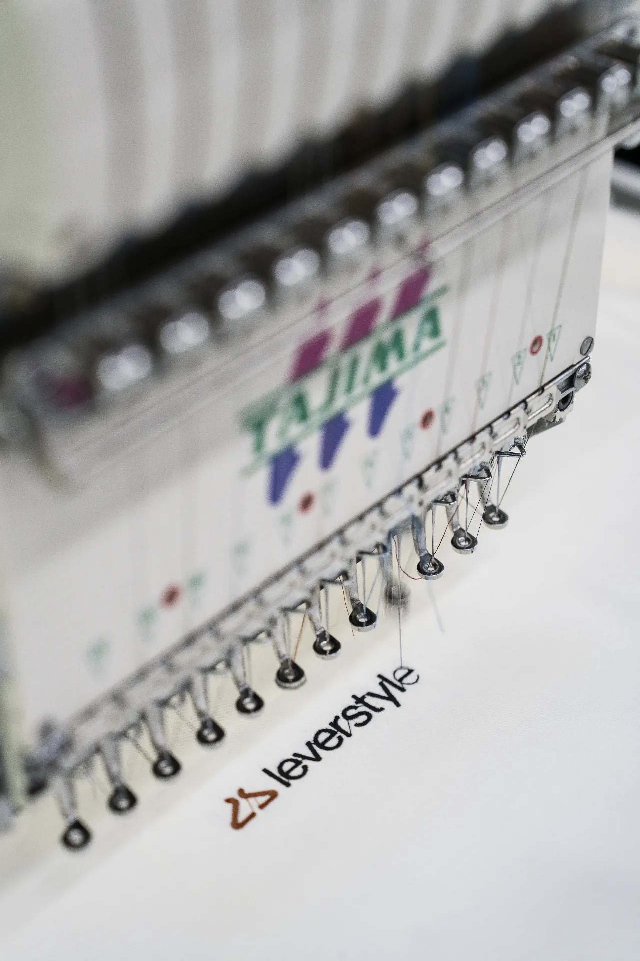 Embroidery machine stitching the LeverStyle wordmark onto fabric.